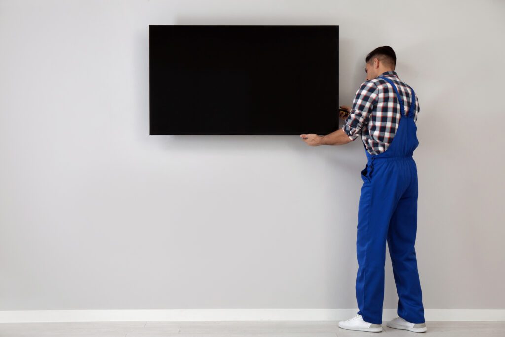 Professional technician with screwdriver adjusting the TV and securing it after mounting it.