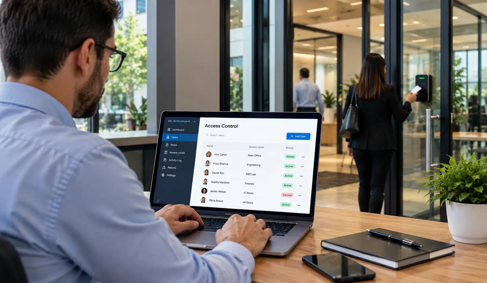 Office manager reviewing employee access permissions on a laptop while an employee uses a door access reader.